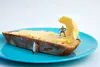 A staged photographic print of mini figures surfing on butter and bread by New Zealand artist Adam Popovic, available at The Little Gallery Tairua